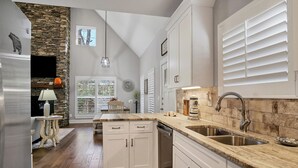A kitchen with white cabinets, a stone accent wall, a built-in oven, and a large window with blinds. - Beautiful mountain home with modern features Gas fire-place on the screened deck (Townsend)