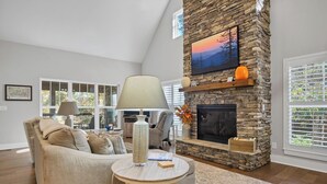 A living room with a stone fireplace, a sofa, a coffee table, and a large window. - Beautiful mountain home with modern features Gas fire-place on the screened deck (Townsend)