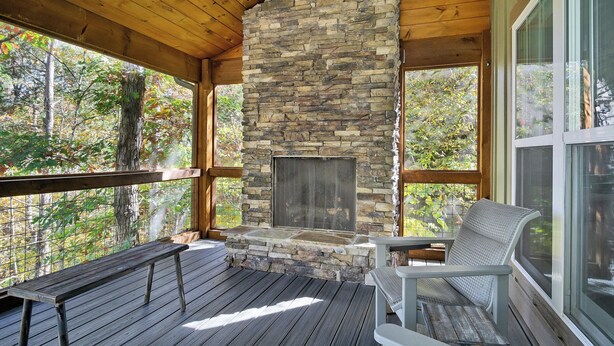 A stone fireplace with a screened glass door, wooden deck, and seating area. - Beautiful mountain home with modern features Gas fire-place on the screened deck (Townsend)