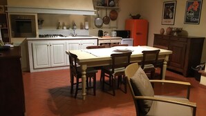 Une cuisine avec des meubles blancs, une table à manger avec des chaises, un réfrigérateur rouge et un sol carrelé.