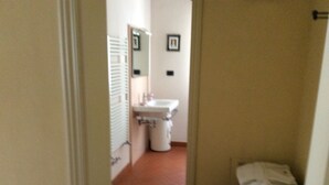 Un couloir étroit avec un lavabo blanc et une poubelle.