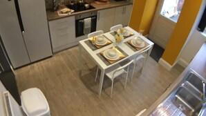 Een kleine keuken met een eethoek, een klok aan de muur en uitzicht op buiten.