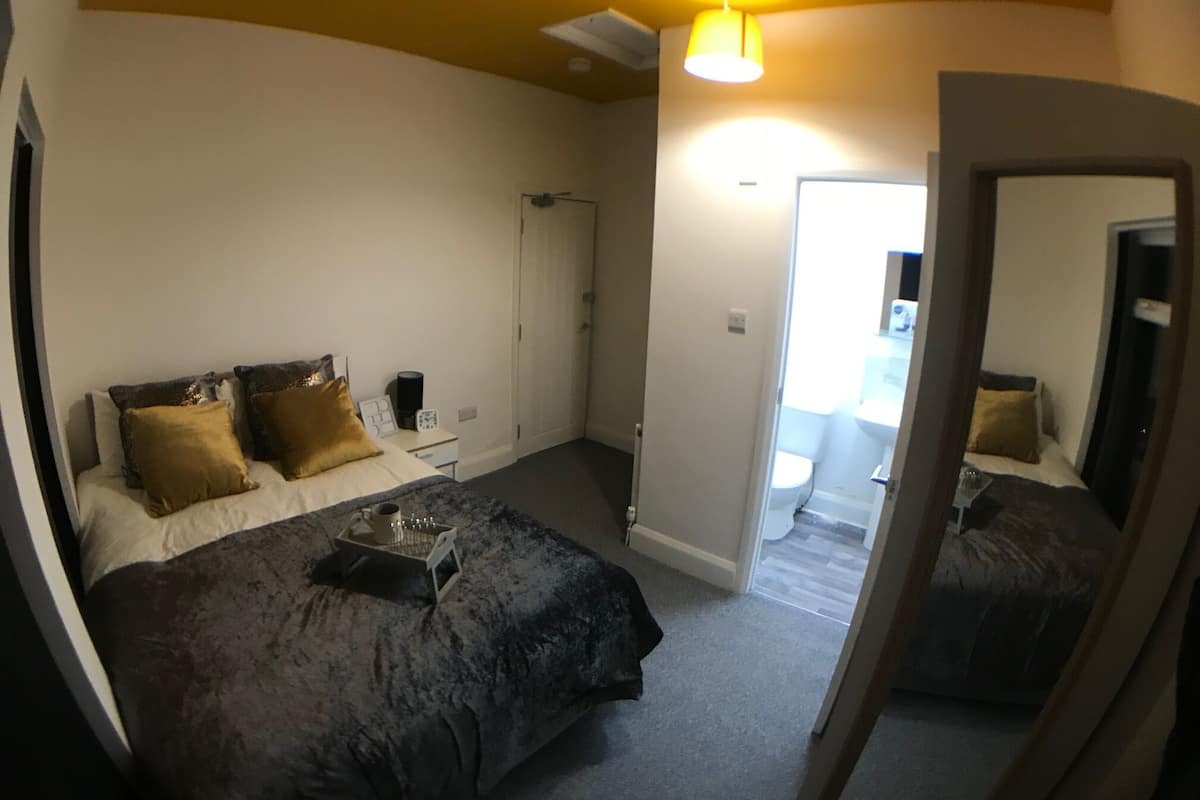 Une chambre à coucher comprenant un lit, une table de chevet, une lampe et une porte donnant sur une salle de bain.