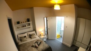 Een slaapkamer met een bed, nachtkastje, lamp en een deur naar een badkamer.
