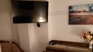 Una sala de estar con un televisor de pantalla plana en la pared, un piano de madera, un sillón estampado con motivos florales y una alfombra con diseño.