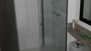 Un baño con ducha de mampara de vidrio, inodoro blanco y encimera de granito con espejo sobre el lavabo.