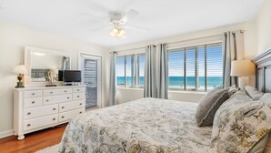 Ein Schlafzimmer mit Bett, Kommode, Fernseher und Fenstern mit Vorhängen.