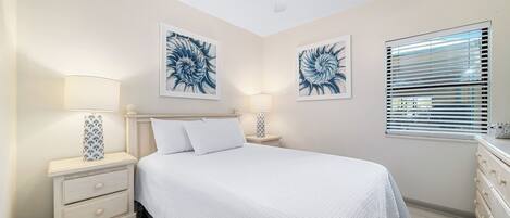 Un dormitorio con cama, dos mesitas de noche con lámparas, un ventilador de techo y obras de arte en las paredes.