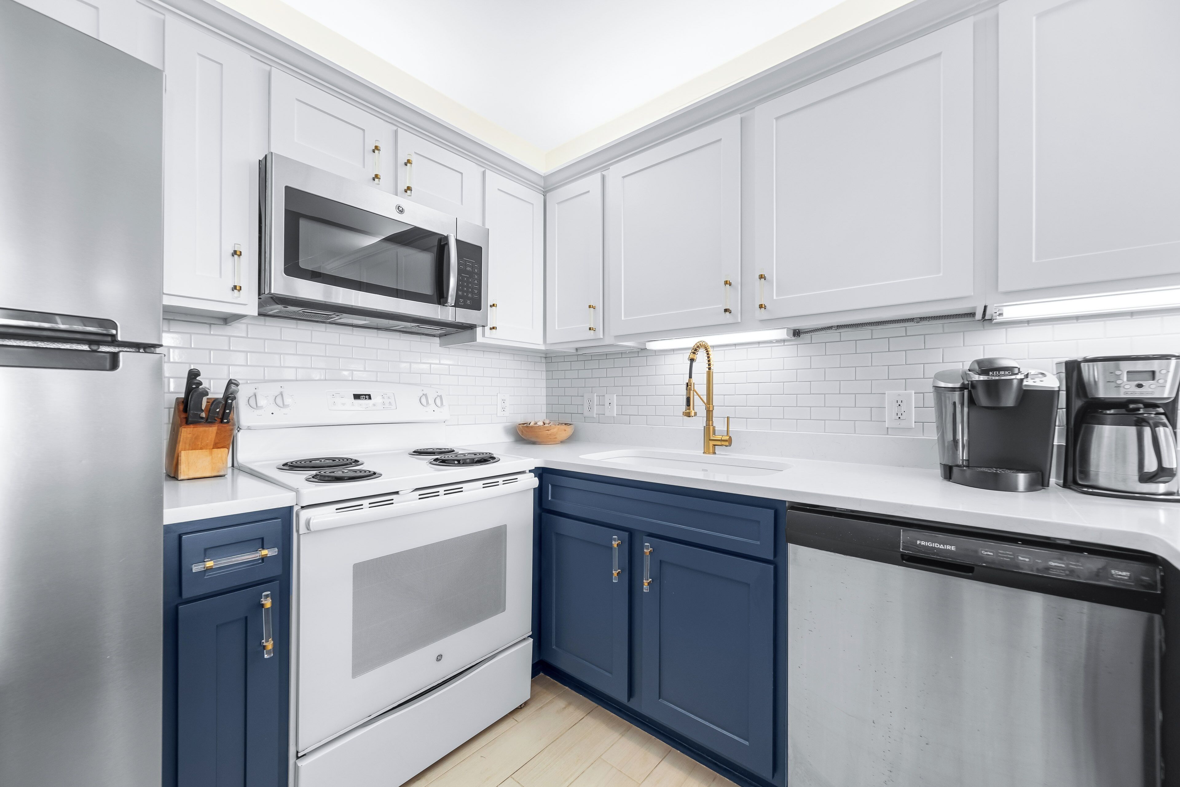 Una cocina moderna con gabinetes blancos, un microondas de acero inoxidable, un horno empotrado y un lavavajillas.