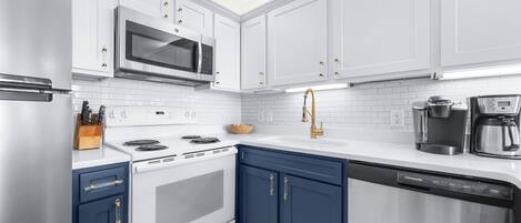Una cocina moderna con gabinetes blancos, un microondas de acero inoxidable, un horno empotrado y un lavavajillas.
