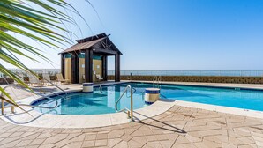 A swimming pool with a wooden deck, lounge chairs, and a view of the ocean.