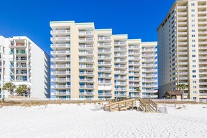 Un hotel frente a la playa con varios pisos, balcones y una zona de arena.