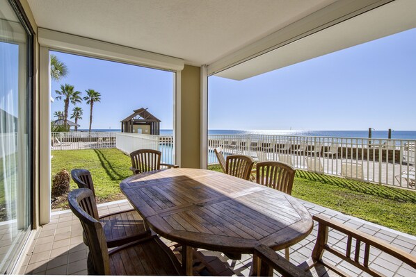 Una mesa y sillas de madera en un balcón con vista a la playa y el océano.