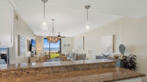 A spacious kitchen with granite countertops, a dining area with a view, and a living room with a large window overlooking the ocean. - Romar Place 104 |  Beachfront Condo | Indoor & Outdoor Pools | Beach Getaways (Orange Beach)