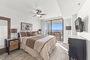 Un dormitorio con cama, ventilador de techo, televisión y balcón con vistas.