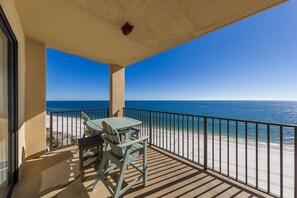 A balcony with a table and chairs, overlooking a beach and ocean.