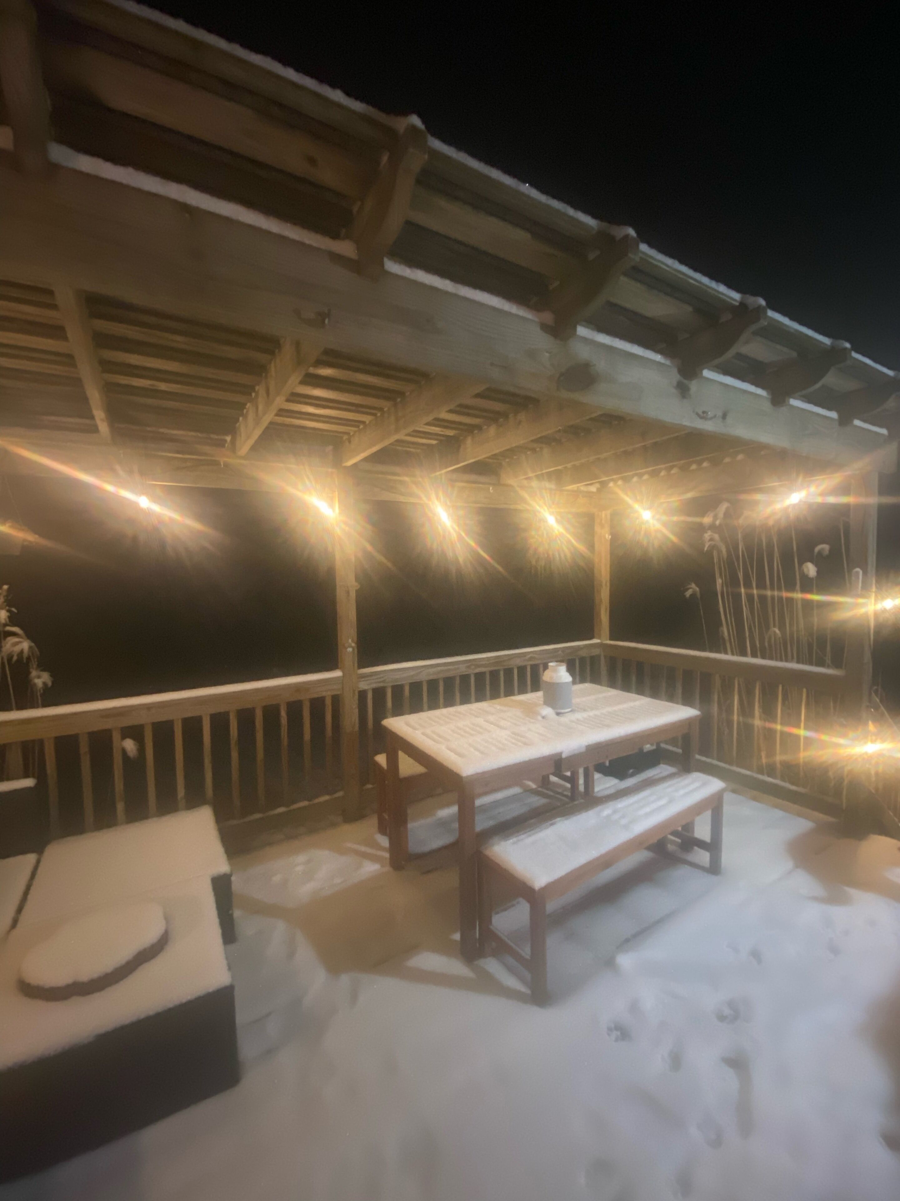 An outdoor patio with a wooden table and bench, surrounded by a railing.