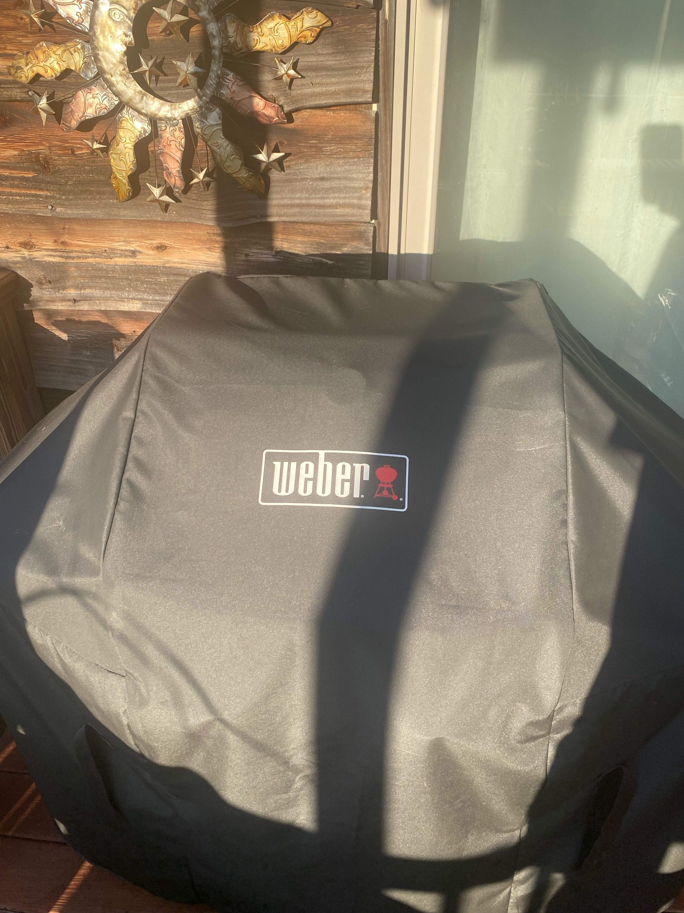 A covered object with a "Weber" logo, a decorative metal piece, and a wooden background.