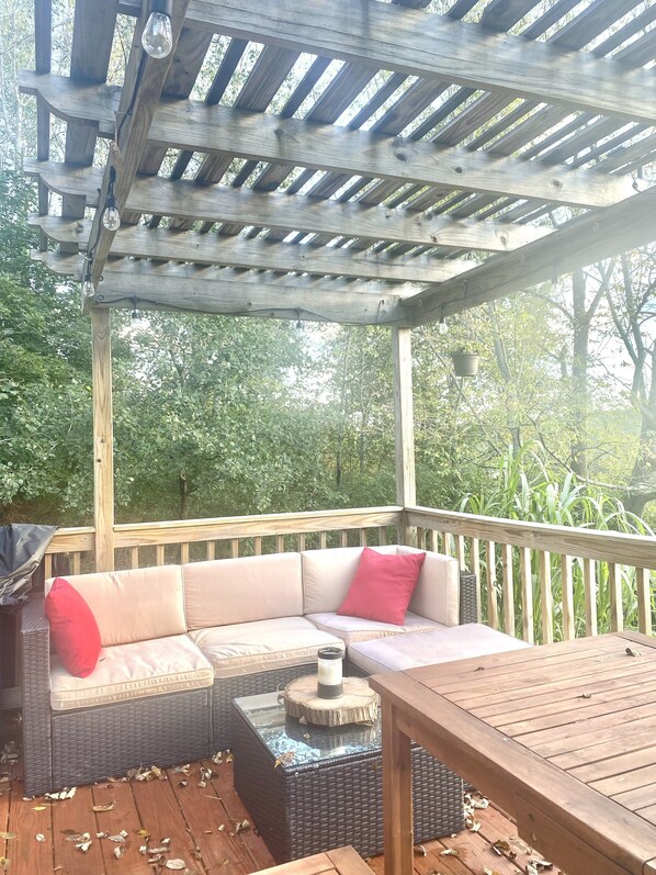 Un espacio de estar al aire libre techado con un banco de madera, un sofá acolchado y una mesa.