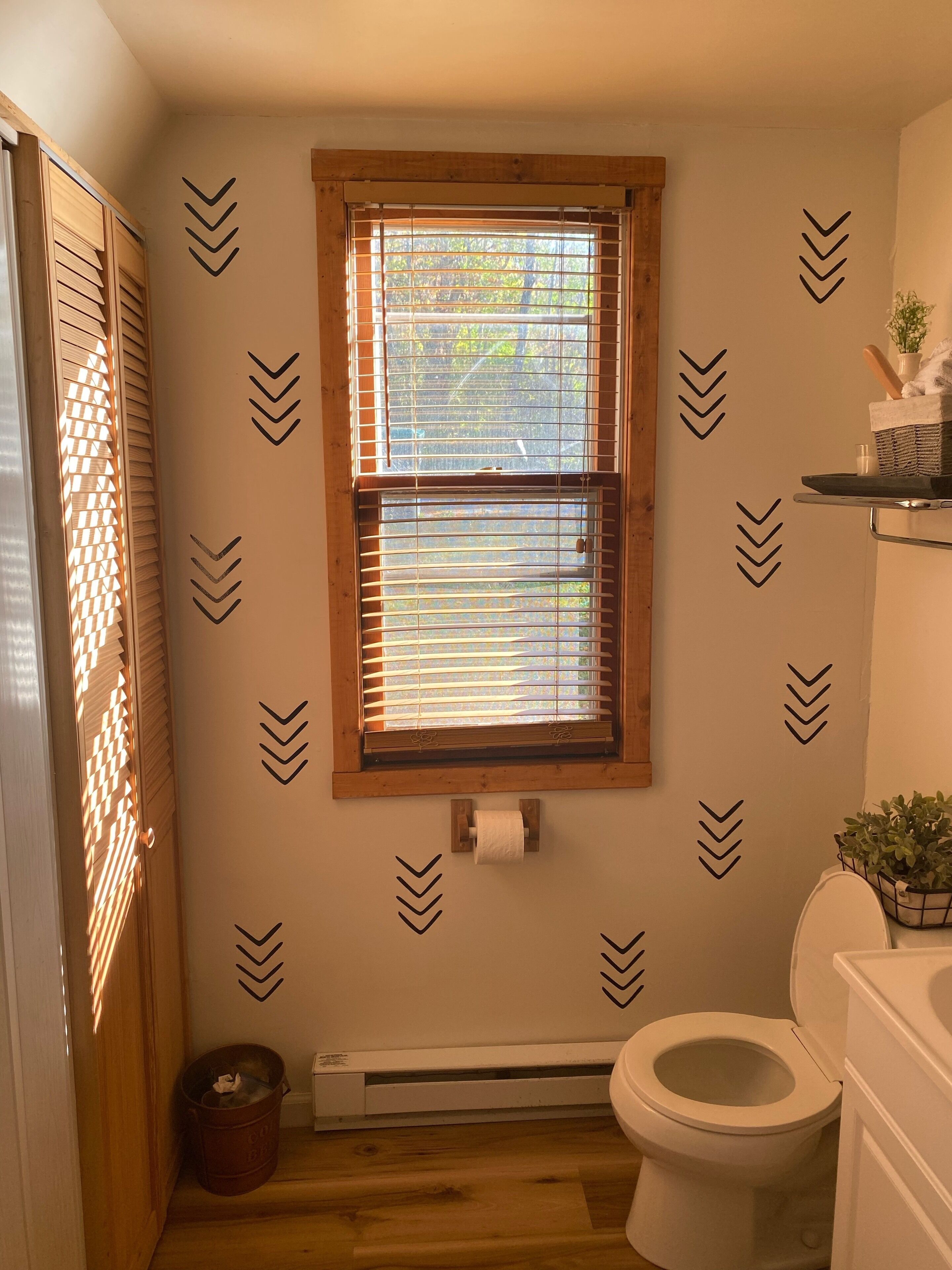 Ein Badezimmer mit Toilette, einem Fenster mit Jalousien, einem Handtuchhalter und einer kleinen Pflanze.