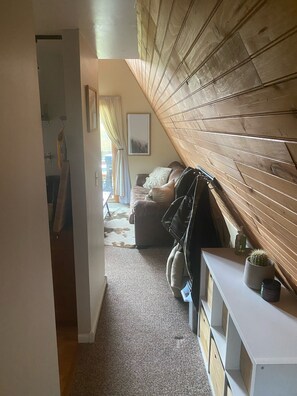 Tunnelmallinen huone, jossa on kalteva katto, sohva, pieni pöytä, jonka päällä on kaktus, ja naulakko.