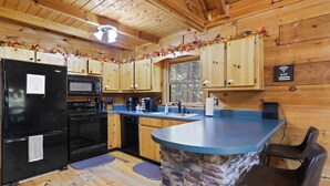 A wooden cabin kitchen with a stone island, black appliances, and a view of the forest. - Dog-Friendly! Secluded Cabin! Only 10 mins to downtown! Hot Tub & Game Room (Blue Ridge)