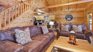 A cabin interior with a wooden staircase, leather sofas, a dining table, and a kitchen area. - Dog-Friendly! Secluded Cabin! Only 10 mins to downtown! Hot Tub & Game Room (Blue Ridge)