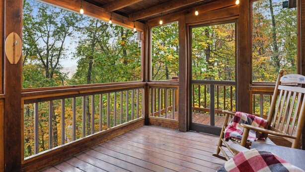 A wooden deck with a view of autumn trees, a rocking chair, and a wooden railing. - Dog-Friendly! Secluded Cabin! Only 10 mins to downtown! Hot Tub & Game Room (Blue Ridge)