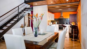 A modern kitchen with a central island, a dining area with a glass table, and a staircase leading to an upper level.