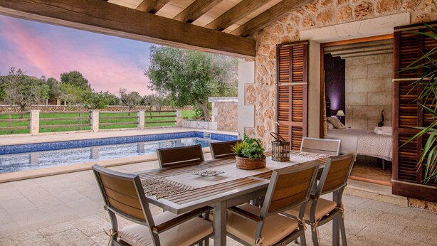 An outdoor patio with a pool, wooden furniture, and a stone wall.