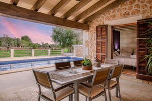 An outdoor patio with a pool, wooden furniture, and a stone wall. - YourHouse Can Cuixa, villa with private pool, Majorca north (Santa Margalida)