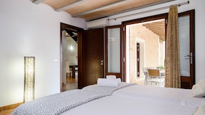 A bedroom with a large bed, a wooden door leading to a balcony, and a small table with chairs outside.