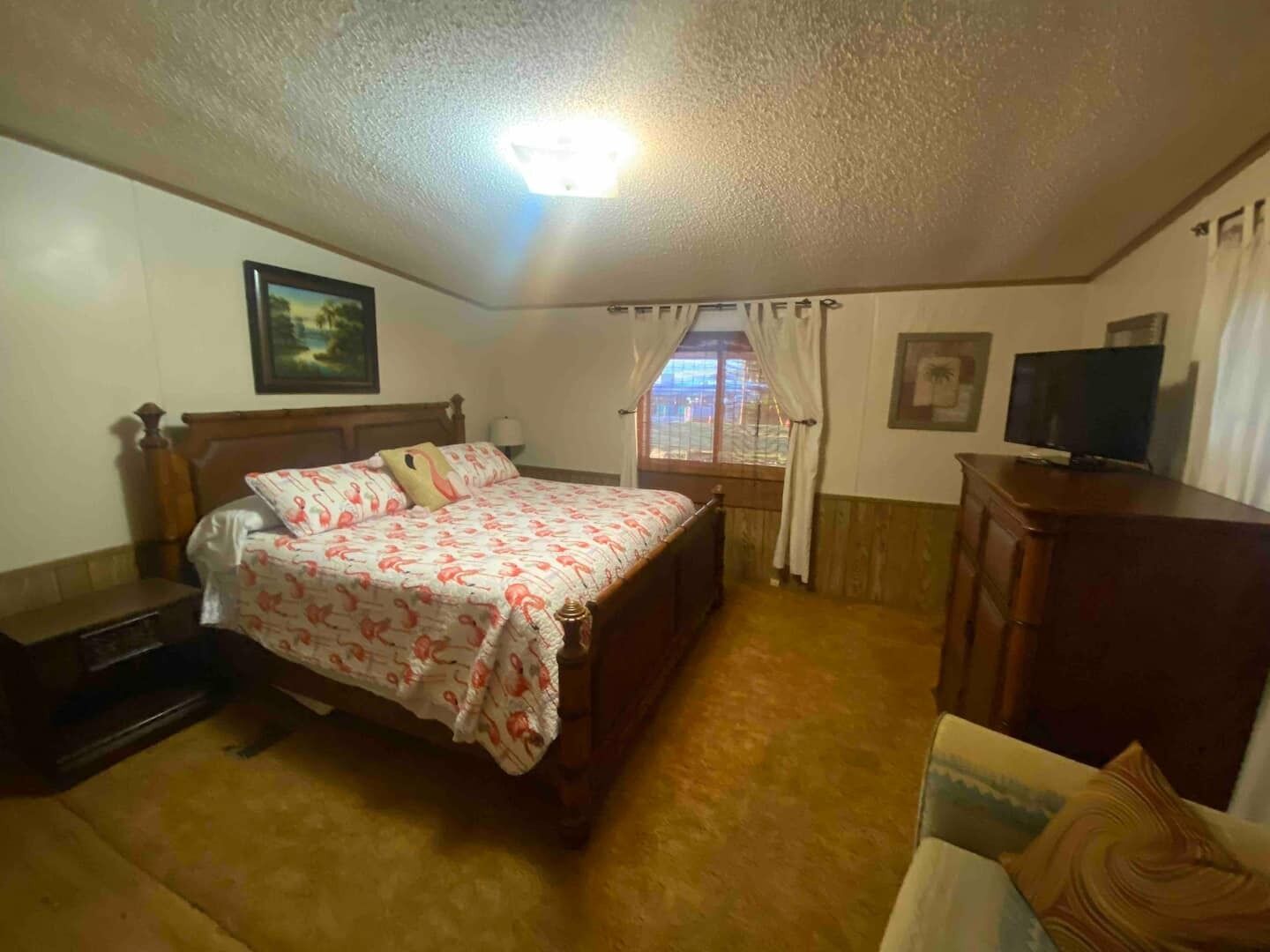 Un dormitorio con cama, televisión, escritorio y ventana con cortinas.