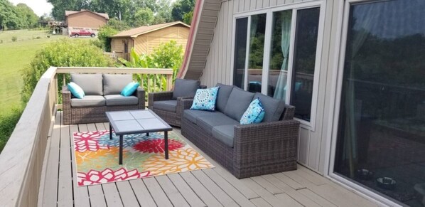 A deck with wicker furniture, a table, and a colorful rug.