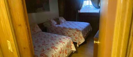 Un pasillo estrecho que conduce a un dormitorio con dos camas, suelo de madera y una ventana con cortinas.