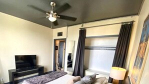 Ein modernes Hotelzimmer mit Bett, Fernseher, Deckenventilator und einem Fenster mit Vorhängen.