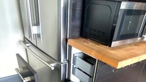 Eine Küche mit einer Mikrowelle, einem schwarzen Mülleimer und einer Holz Arbeitsplatte.