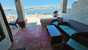 An outdoor patio with a view of a lake, a sofa, a table, and a chair.