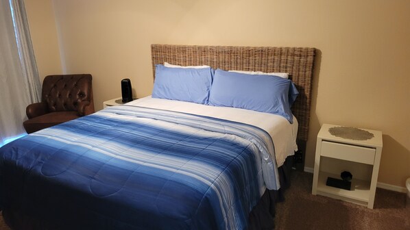 A bedroom with a bed, a chair, a nightstand, and a small bedside table.