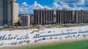A beachfront hotel with multiple high-rise buildings, a sandy beach with numerous umbrellas, and a clear blue sky. - Beachfront Condo w Private Balcony in Orange Beach, AL at PHX I (Orange Beach)