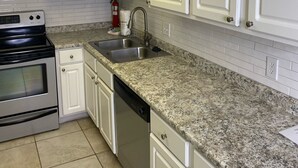 A kitchen with white cabinets, a granite countertop, stainless steel appliances, and a tiled backsplash. - Beachfront Condo w Private Balcony in Orange Beach, AL at PHX I (Orange Beach)