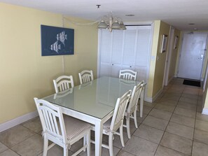 Uma sala de jantar com uma mesa de vidro, cadeiras brancas, um lustre e um quadro na parede.