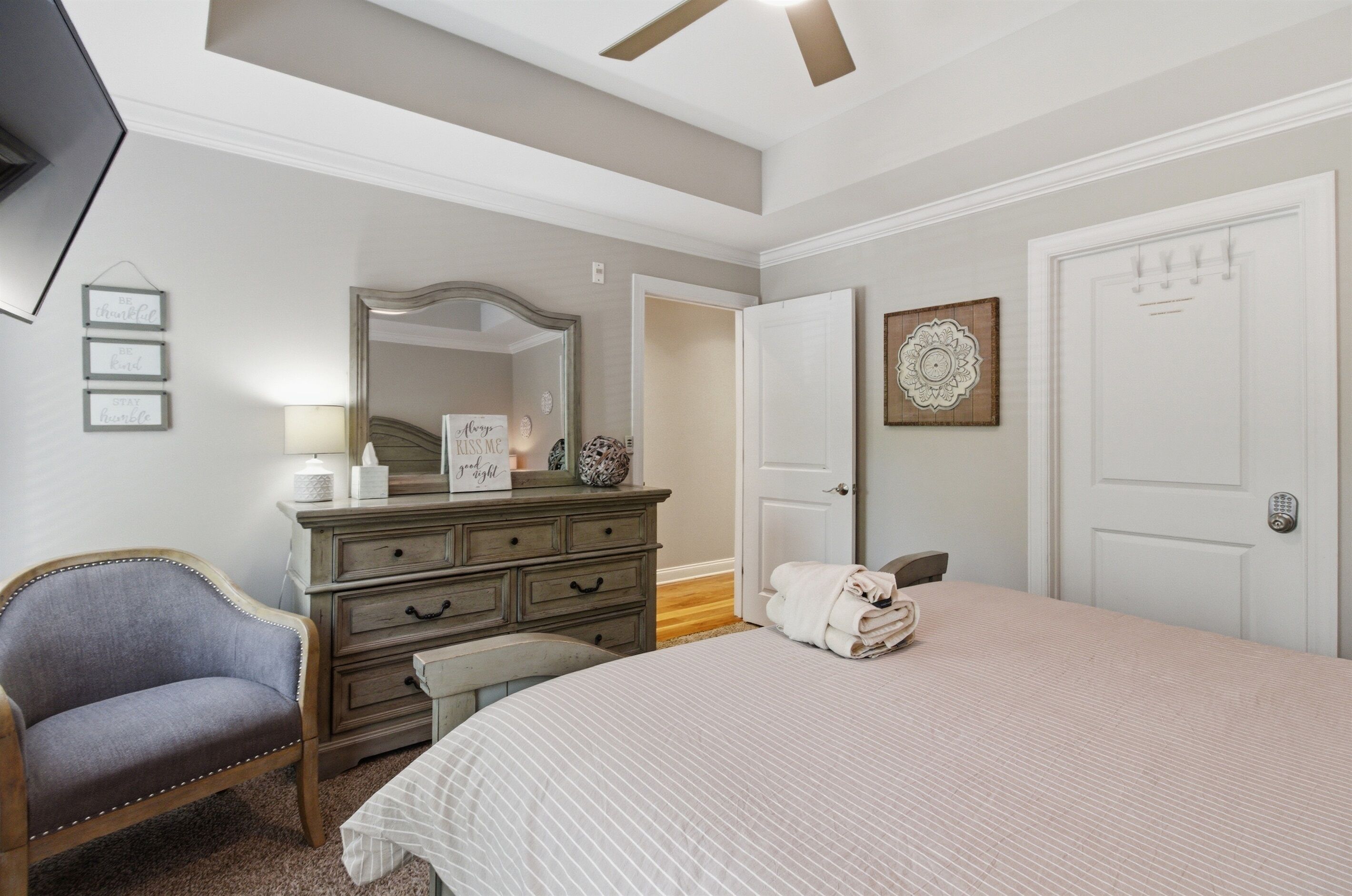 Une chambre à coucher avec un lit, une commode, une chaise, un miroir et une porte.