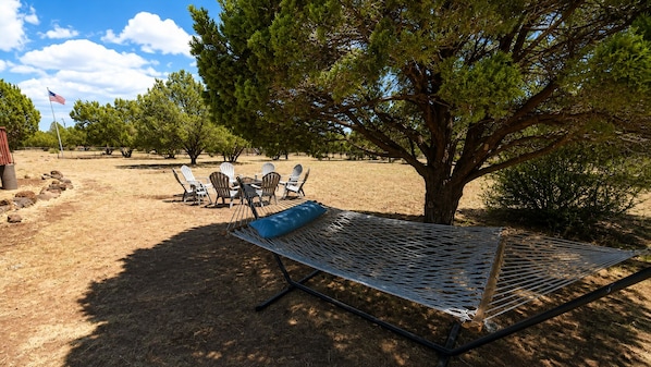 A hammock under a tree, a picnic table with chairs, and a flag.