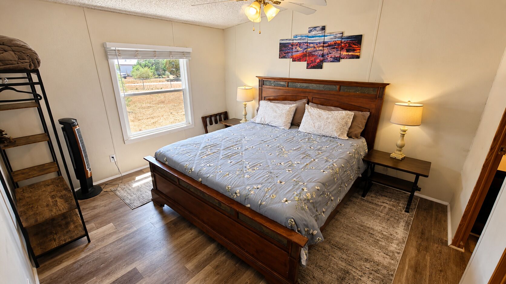 Un dormitorio con cama de madera, una ventana, ventilador de techo y una obra de arte en la pared.