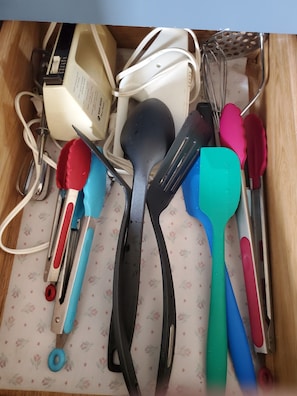 A drawer containing various kitchen utensils including a whisk, spatulas, and a grater.