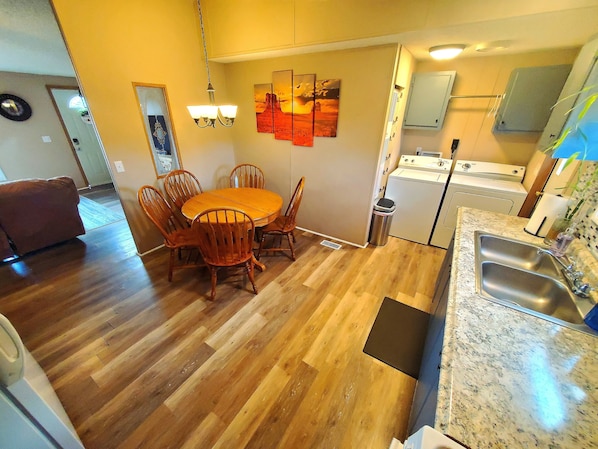 A compact kitchen with a dining area, wooden flooring, and basic amenities including a sink and a washing machine.