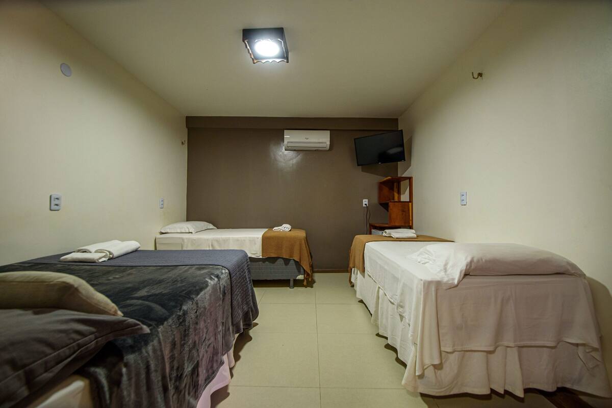 Ein Hotelzimmer mit zwei Betten, einem Fernseher, einer Klimaanlage und einem kleinen Holztisch.