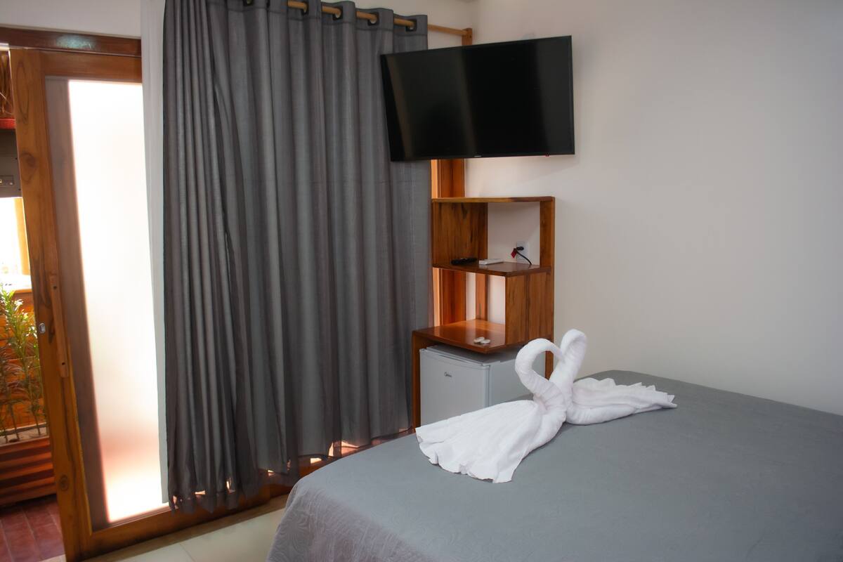 Ein Hotelzimmer mit einem Bett, einem an der Wand montierten Flachbildfernseher, einem Nachttisch aus Holz und einem kleinen Schrank.