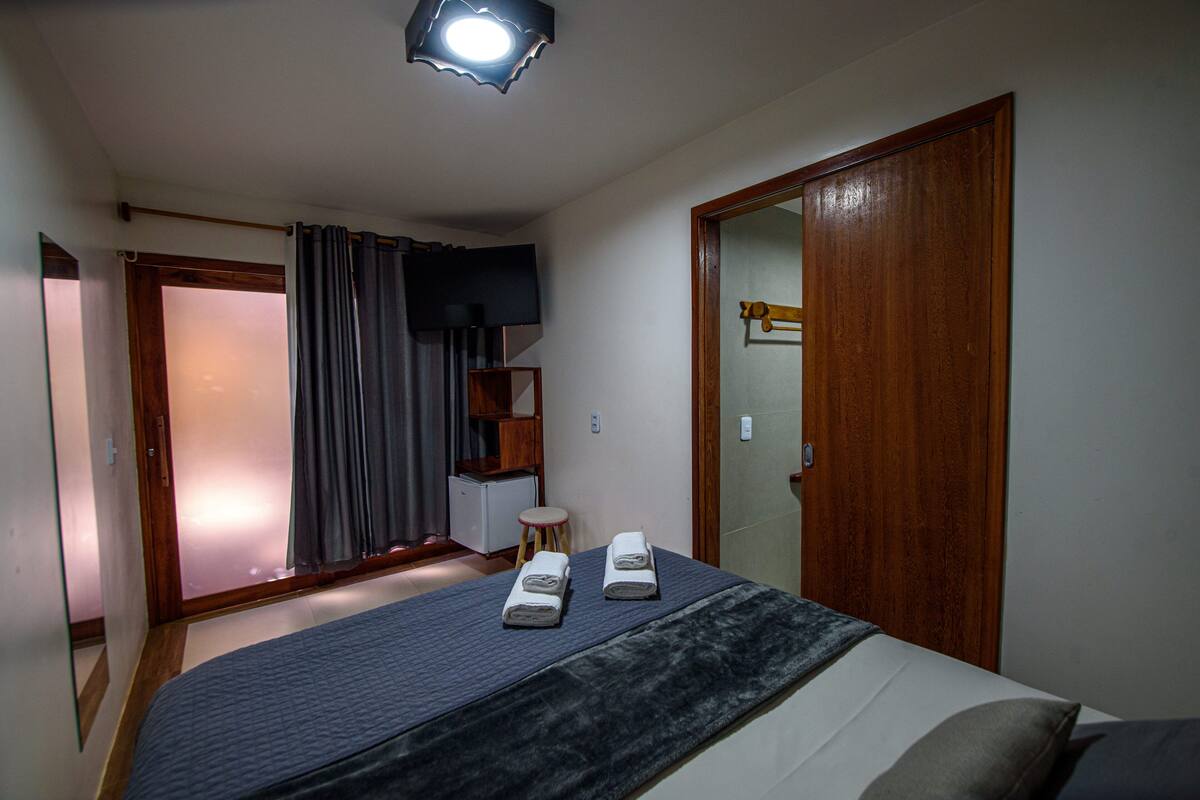 Ein Schlafzimmer mit einem Bett, einem Holzschrank, einem kleinen Hocker und einem Fernseher an der Wand.